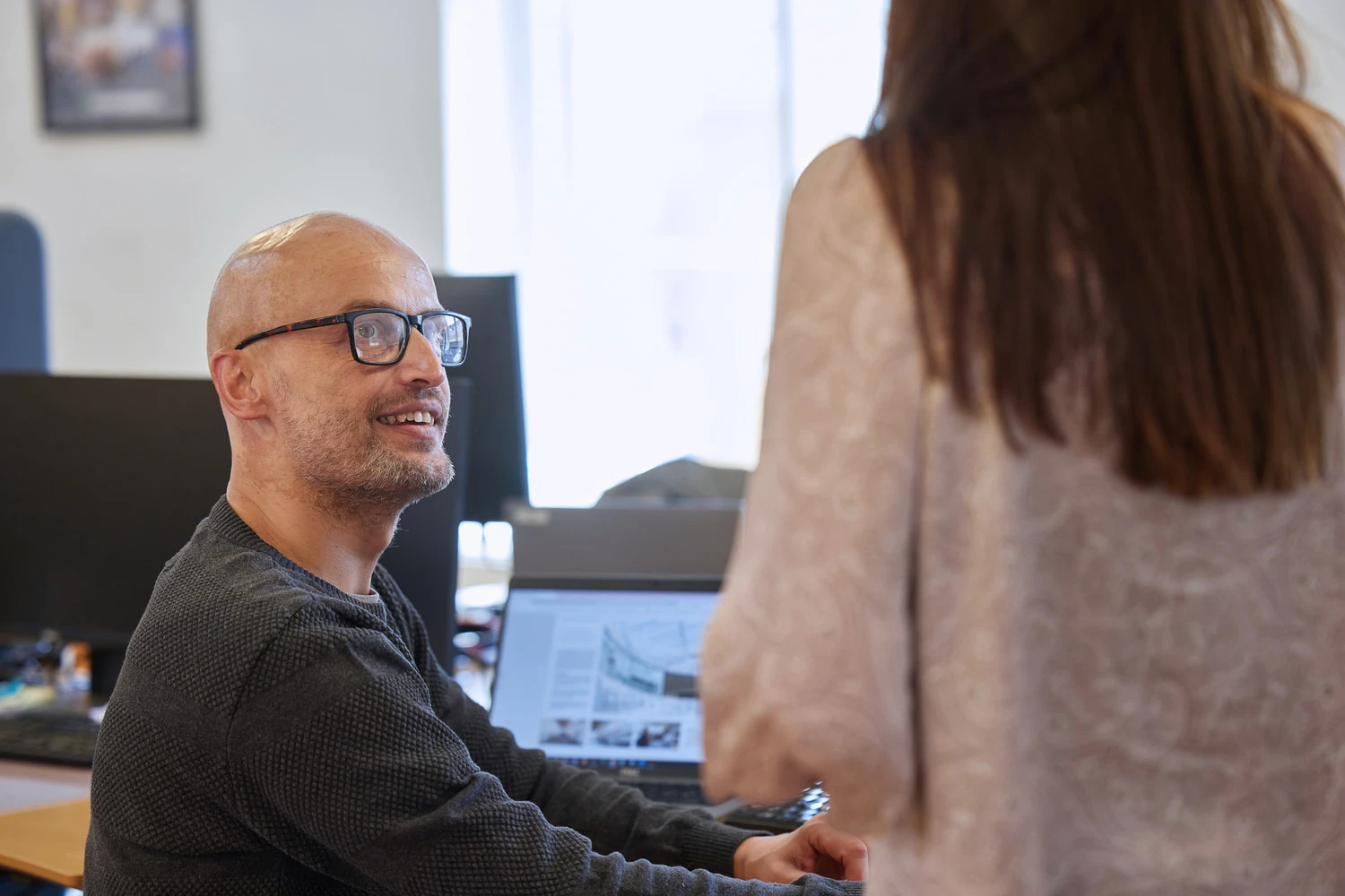 A man is sitting down while looking up at a woman who is talking to him at JS Danmark.